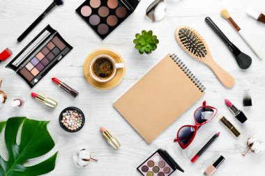 Beyaz ofis masasında kadın kozmetik ürünleri. Laptop, not defteri, ruj, pudra, tarak, kadın mücevherleri. Üst Manzara. Metnin için boş yer. Düz yatıyordu.