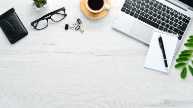 Boş defterli beyaz ofis masası, bilgisayar klavyesi ve ofis malzemeleri. Kopyalama alanı olan üst görünüm, düz yatay.
