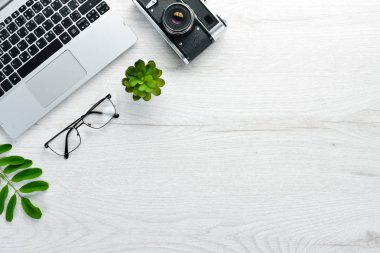 Kamera, dizüstü bilgisayar ve ofis malzemeleriyle dolu beyaz ofis masası. Kopyalama alanı olan üst görünüm, düz yatay.