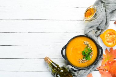 Autumn composition: Pumpkin soup with pumpkin and colored autumn leaves. flat lay. On a white wooden background. Top view. Free space for your text. clipart