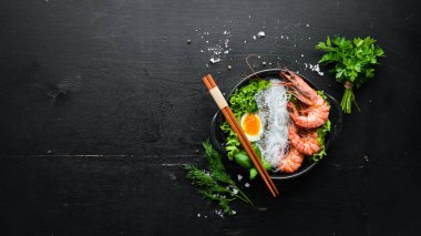 Siyah taşlı arka planda siyah tabakta karidesli erişte, yumurta ve yeşillik. Üst Manzara. Metnin için boş yer.