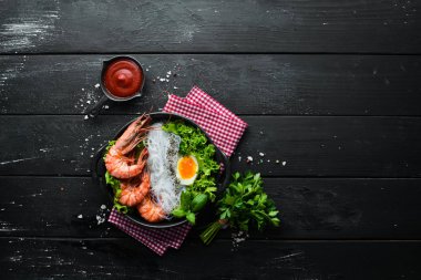 Siyah taşlı arka planda siyah tabakta karidesli erişte, yumurta ve yeşillik. Üst Manzara. Metnin için boş yer.