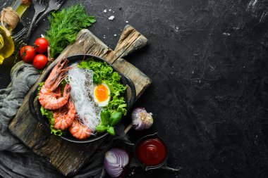 Siyah taşlı arka planda siyah tabakta karidesli erişte, yumurta ve yeşillik. Üst Manzara. Metnin için boş yer.