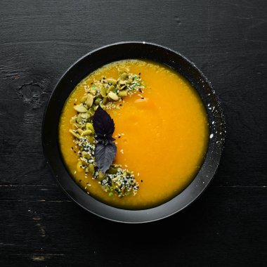 Beyaz ahşap arka planda siyah bir tabakta kabak tohumlu balkabağı çorbası. Üst Manzara. Metnin için boş yer.