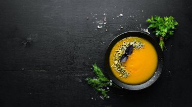 Beyaz ahşap arka planda siyah bir tabakta kabak tohumlu balkabağı çorbası. Üst Manzara. Metnin için boş yer.