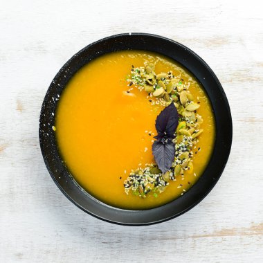 Beyaz ahşap arka planda siyah bir tabakta kabak tohumlu balkabağı çorbası. Üst Manzara. Metnin için boş yer.