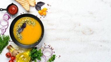 Beyaz ahşap arka planda siyah bir tabakta kabak tohumlu balkabağı çorbası. Üst Manzara. Metnin için boş yer.