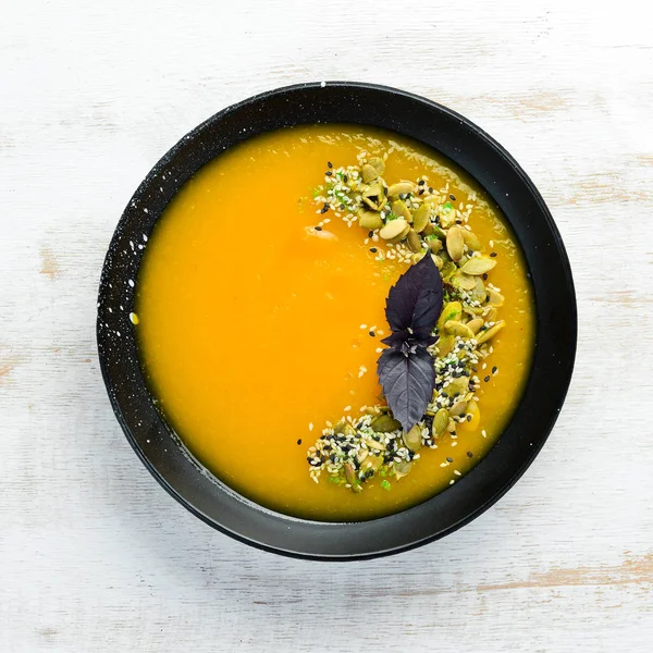 Pumpkin soup with pumpkin seeds in a black plate on a white wooden background. Top view. Free space for your text.