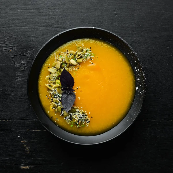 Pumpkin soup with pumpkin seeds in a black plate on a white wooden background. Top view. Free space for your text. — Stock Image Pumpkin Soup Pumpkin Seeds Black Plate White Wooden Background Top Stock Image