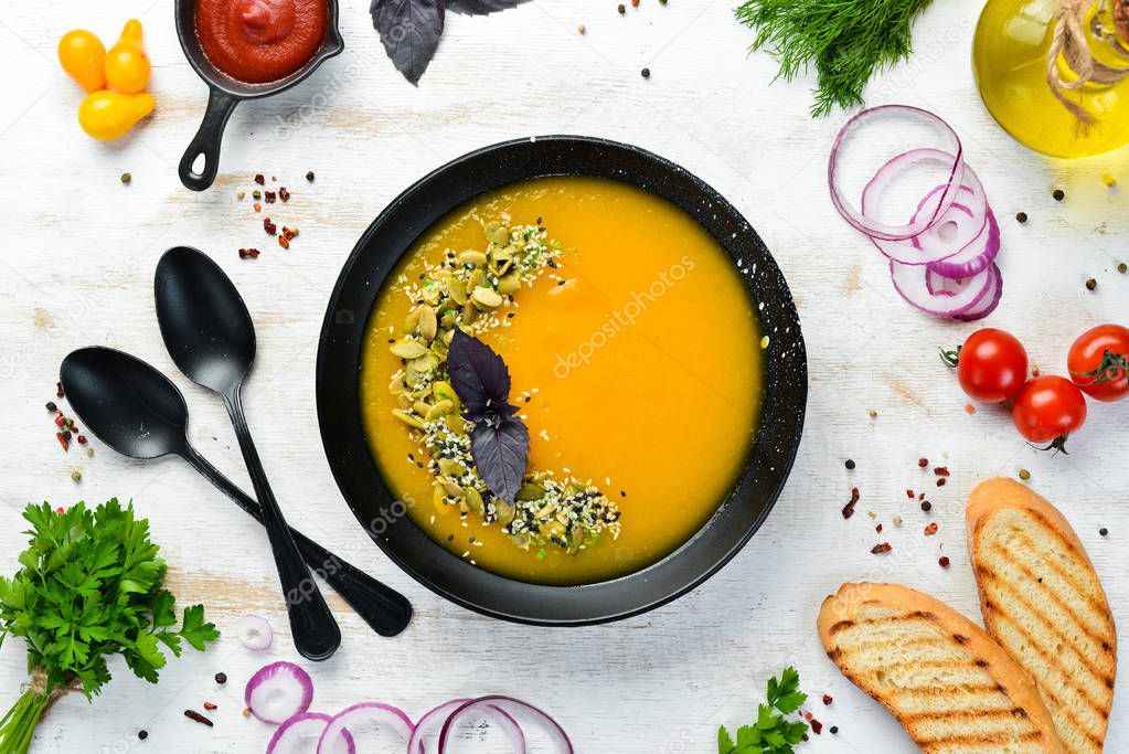 Pumpkin soup with pumpkin seeds in a black plate on a white wooden background. Top view. Free space for your text.