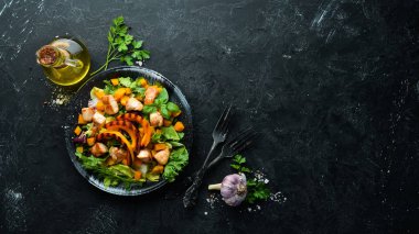 Beyaz ahşap arka planda siyah tabakta tavuk eti ve sebzeli balkabağı salatası. Üst Manzara. Metnin için boş yer.