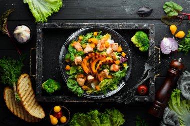 Beyaz ahşap arka planda siyah tabakta tavuk eti ve sebzeli balkabağı salatası. Üst Manzara. Metnin için boş yer.