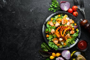 Beyaz ahşap arka planda siyah tabakta tavuk eti ve sebzeli balkabağı salatası. Üst Manzara. Metnin için boş yer.
