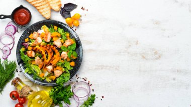 Beyaz ahşap arka planda siyah tabakta tavuk eti ve sebzeli balkabağı salatası. Üst Manzara. Metnin için boş yer.