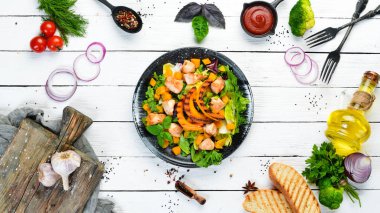 Beyaz ahşap arka planda siyah tabakta tavuk eti ve sebzeli balkabağı salatası. Üst Manzara. Metnin için boş yer.