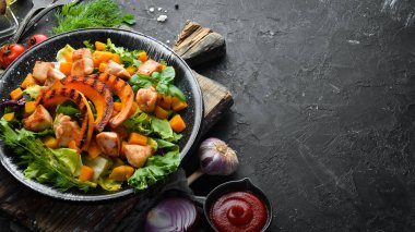 Beyaz ahşap arka planda siyah tabakta tavuk eti ve sebzeli balkabağı salatası. Üst Manzara. Metnin için boş yer.