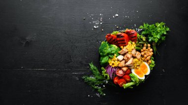 Buda kasesi: Tavuk, nohut, brokoli, domates, yumurta, kırmızı biber, siyah arkaplanda siyah bir tabakta soğan. Üst Manzara. Metnin için boş yer.
