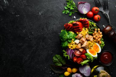 Buda kasesi: Tavuk, nohut, brokoli, domates, yumurta, kırmızı biber, siyah arkaplanda siyah bir tabakta soğan. Üst Manzara. Metnin için boş yer.