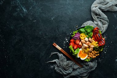 Buda kasesi: Tavuk, nohut, brokoli, domates, yumurta, kırmızı biber, siyah arkaplanda siyah bir tabakta soğan. Üst Manzara. Metnin için boş yer.