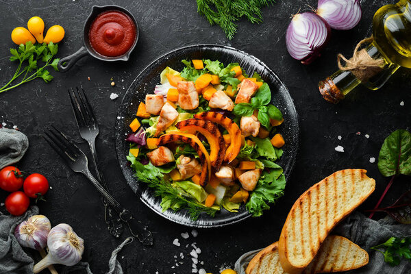 Салат из тыквы с куриным мясом и овощами в черной тарелке на белом деревянном фоне. Вид сверху. Свободное место для текста
.