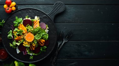 Salata: pancar, balkabağı, mısır ve marul beyaz ahşap arka planda siyah bir tabakta. Üst Manzara. Metnin için boş yer.