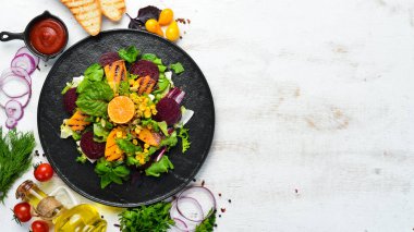 Salata: pancar, balkabağı, mısır ve marul beyaz ahşap arka planda siyah bir tabakta. Üst Manzara. Metnin için boş yer.