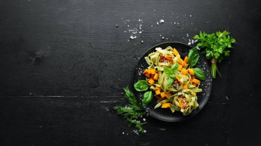 Siyah arka planda siyah tabakta balkabaklı makarna ve ıspanak. Üst Manzara. Metnin için boş yer.