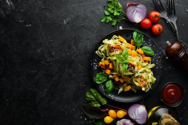 Siyah arka planda siyah tabakta balkabaklı makarna ve ıspanak. Üst Manzara. Metnin için boş yer.