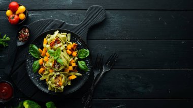 Siyah arka planda siyah tabakta balkabaklı makarna ve ıspanak. Üst Manzara. Metnin için boş yer.