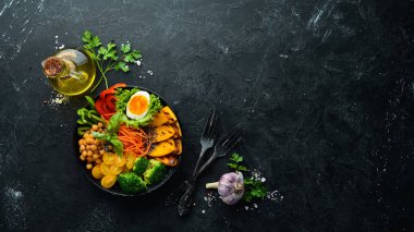 Buda kasesi: balkabağı, brokoli, yumurta, domates, havuç, beyaz ahşap zemin üzerinde siyah bir tabakta kırmızı biber. Üst Manzara. Metnin için boş yer.