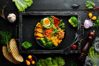 Buda kasesi: balkabağı, brokoli, yumurta, domates, havuç, beyaz ahşap zemin üzerinde siyah bir tabakta kırmızı biber. Üst Manzara. Metnin için boş yer.