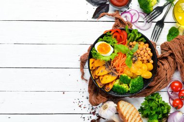 Buda kasesi: balkabağı, brokoli, yumurta, domates, havuç, beyaz ahşap zemin üzerinde siyah bir tabakta kırmızı biber. Üst Manzara. Metnin için boş yer.