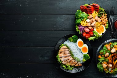 Siyah arka planda siyah tabakta tavuk eti ve sebze tabakları. Buda kasesi. Üst Manzara. Metnin için boş yer.