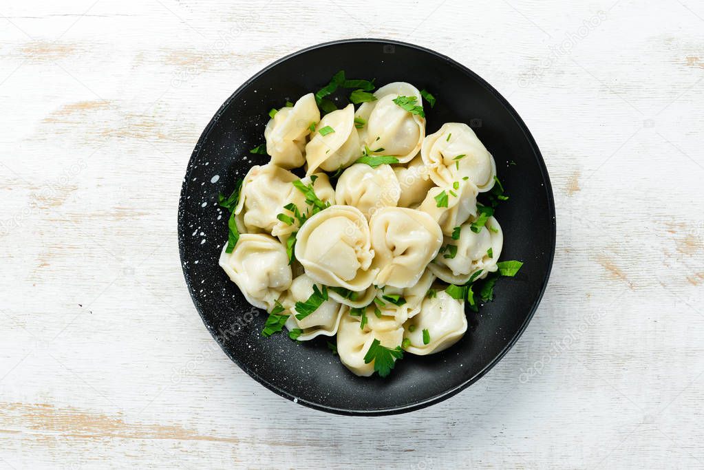 Russian pelmeni meat Dumplings with greens in a black plate. Russian traditional cuisine. Top view. Free copy space.