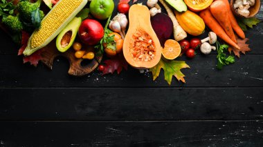Siyah bir arka planda sonbahar sebzeleri: balkabağı, domates, mısır, salatalık, soğan, havuç. Sonbahar yemeği. Üst Manzara. Boş kopyalama alanı.