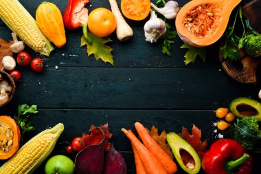 Siyah taş zemin üzerinde taze mevsimlik sebzeler: balkabağı, domates, avokado, salatalık, soğan, havuç. Sonbahar yemeği. Üst Manzara. Boş kopyalama alanı.