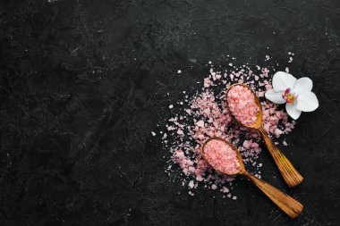 Kaşıkta pembe kokulu deniz tuzu. Siyah taştan bir arka planda. Spa tedavileri. Üst Manzara. Metnin için boş yer.