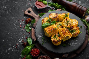Yiyecekler. Siyah taş tabakta maydanozlu ve fesleğenli fırında mısır. Üst Manzara. Metnin için boş yer.