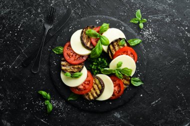 Fesleğenli Caprese salatası. Siyah taş tabakta domates, mozarella peyniri ve patlıcan. Üst Manzara. Metnin için boş yer.