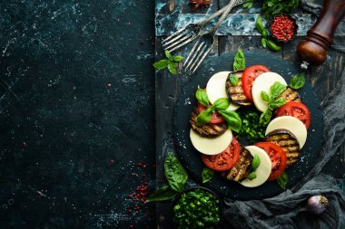 Fesleğenli Caprese salatası. Siyah taş tabakta domates, mozarella peyniri ve patlıcan. Üst Manzara. Metnin için boş yer.