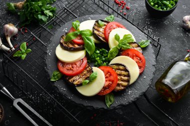 Fesleğenli Caprese salatası. Siyah taş tabakta domates, mozarella peyniri ve patlıcan. Üst Manzara. Metnin için boş yer.