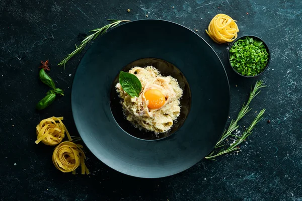 Yumurtalı, parmesan peynirli ve siyah taşlı bir tabakta fesleğenli Carbonara makarnası. Üst Manzara. Kırsal biçim.