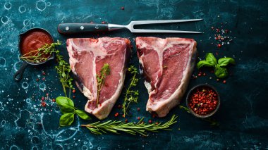 Kemiğin üzerinde çiğ iki biftek ve siyah taşlı bir arka planda baharatlar. Üst Manzara. Kırsal biçim.