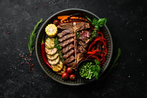 Barbecue. Steak on the bone with grilled vegetables and spices. T-bone steak. Top view. Rustic style.