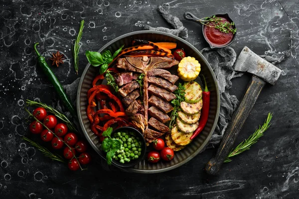 Barbecue. Steak on the bone with grilled vegetables and spices. T-bone steak. Top view. Rustic style.