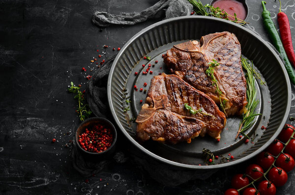 Grilled T-bone steak with spices in a metal baking dish on a black background. Top view. Rustic style.
