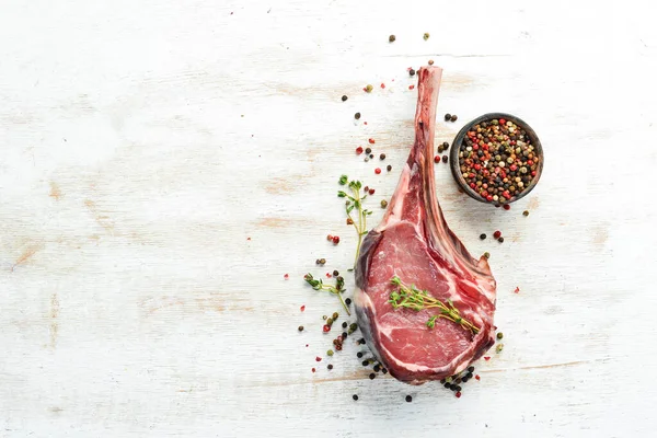 Dry aged raw tomahawk beef steak. Steak on the bone. On a white wooden background. Top view. Free copy space.