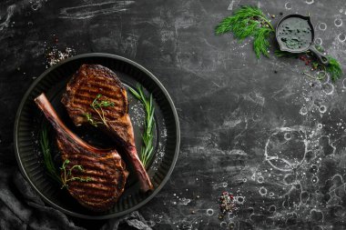 Kemiğe baharat ve otlarla ızgara edilmiş sulu biftek. Siyah taştan bir arka planda. Üst Manzara. Boş kopyalama alanı.