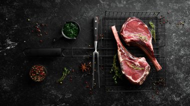 Kemiğe baharatlı iki çiğ biftek. Siyah taştan bir arka planda. Üst Manzara. Boş kopyalama alanı.