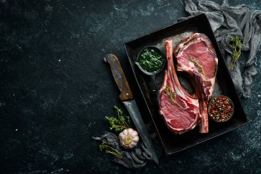 Kemiğe baharatlı iki çiğ biftek. Siyah taştan bir arka planda. Üst Manzara. Boş kopyalama alanı.